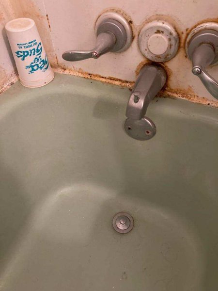 Corroded tub fixtures and failing wall panel before the bathroom remodel